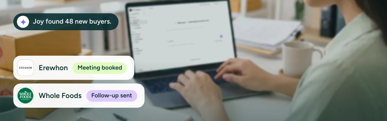 A brand founder at her desk among stacked cartons, typing into Overjoy's AI search on her laptop